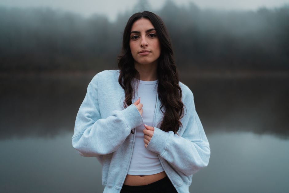 A serene portrait of a woman outdoors, wearing a light blue jacket by a misty lake.