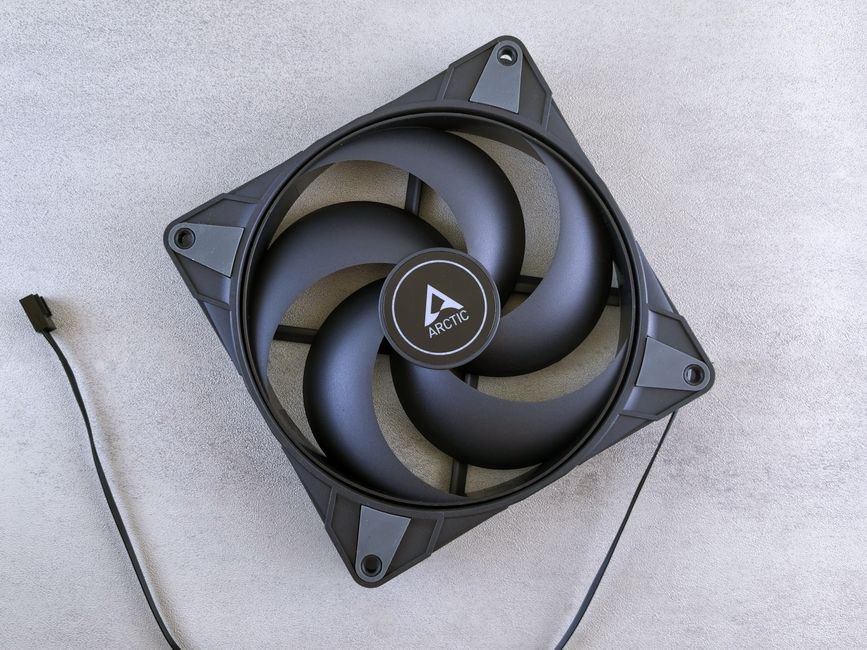 Top view of a black Arctic cooling fan with cable on a grey surface.