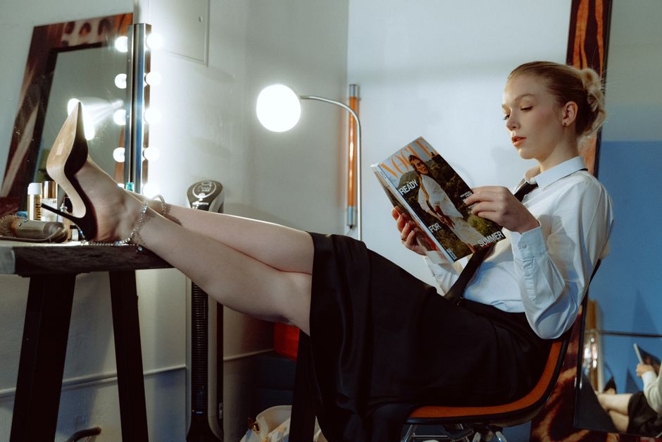 A stylish woman in a dressing room reading a fashion magazine with relaxed legs on the vanity table.