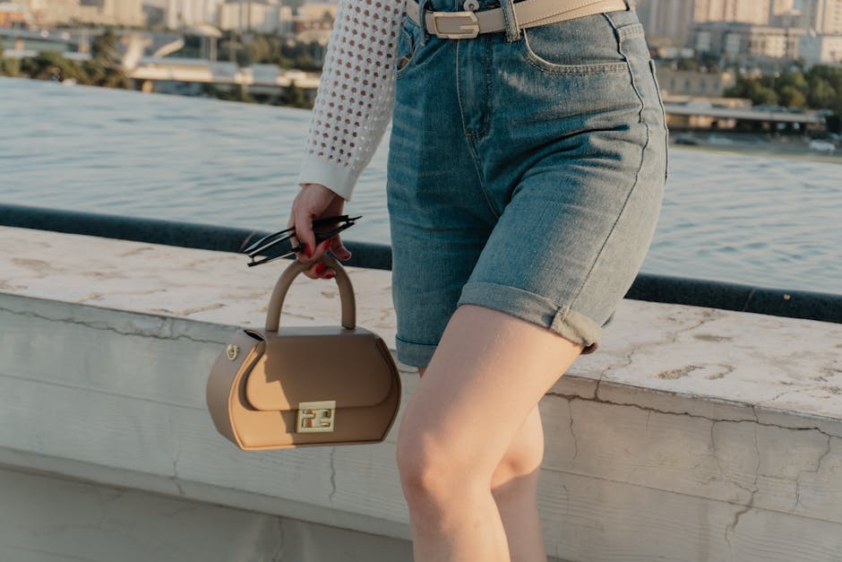 Fashionable woman in denim shorts holding a bag on an urban rooftop with city skyline view.