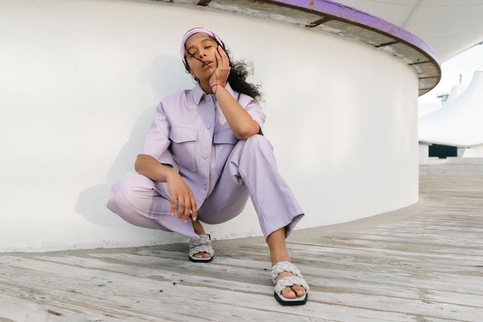 A fashionable woman in lavender attire posing outdoors with hand on cheek, showcasing modern style.