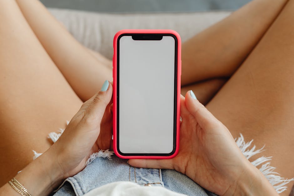 Close-up of a woman holding a smartphone in denim shorts, showcasing the phone display.