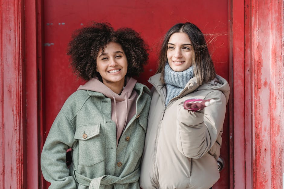Smiling young multiethnic female friends wearing warm clothes while standing and hugging near red building wall in street
