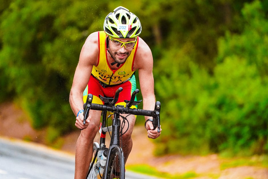Muscular sportsman in t shirt and transparent eyeglasses looking at camera while riding cycle on blurred background