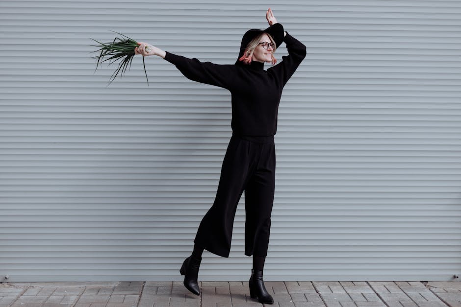 A woman in black jumps energetically holding green leaves against a corrugated backdrop.