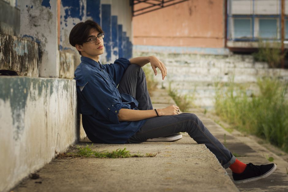 Young man in glasses sitting on steps in an urban area, conveying a relaxed mood.