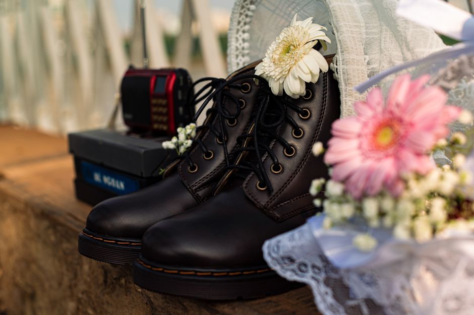 Black leather boots adorned with flowers on a rustic wood surface, conveying a vintage vibe.
