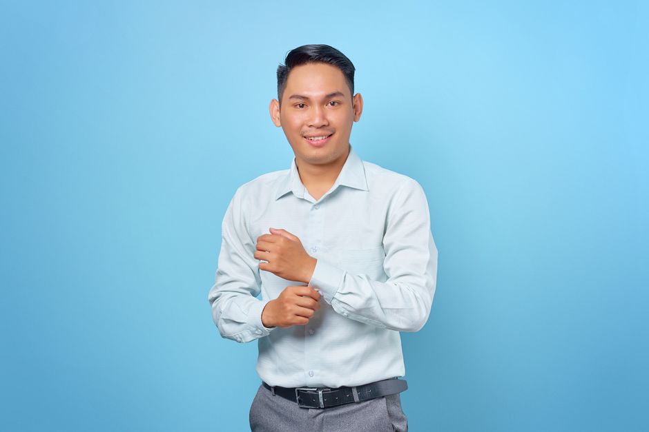 Cheerful young man in a white shirt against a blue background, adjusting his sleeves.