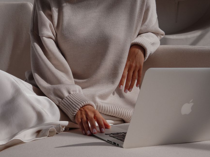 Woman in a cozy sweater using a laptop, showcasing a relaxed and fashionable lifestyle.