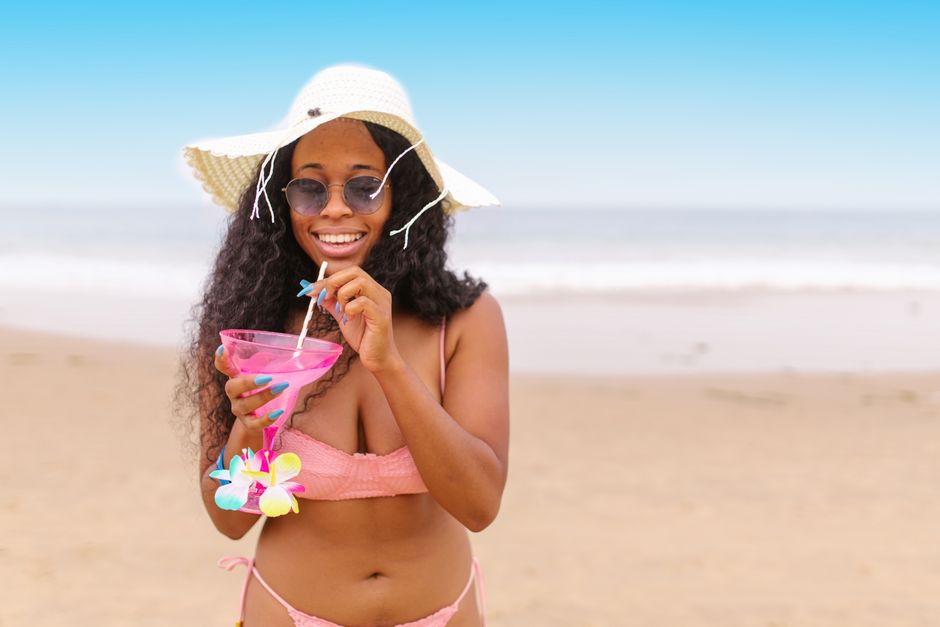 Smiling woman in a swimsuit with a cocktail on a sunny beach vacation.