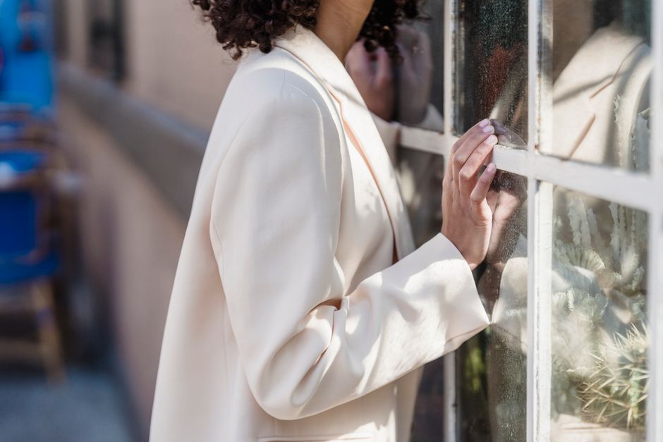 Side view of crop anonymous female with short dark curly hair near window of urban building on blurred background