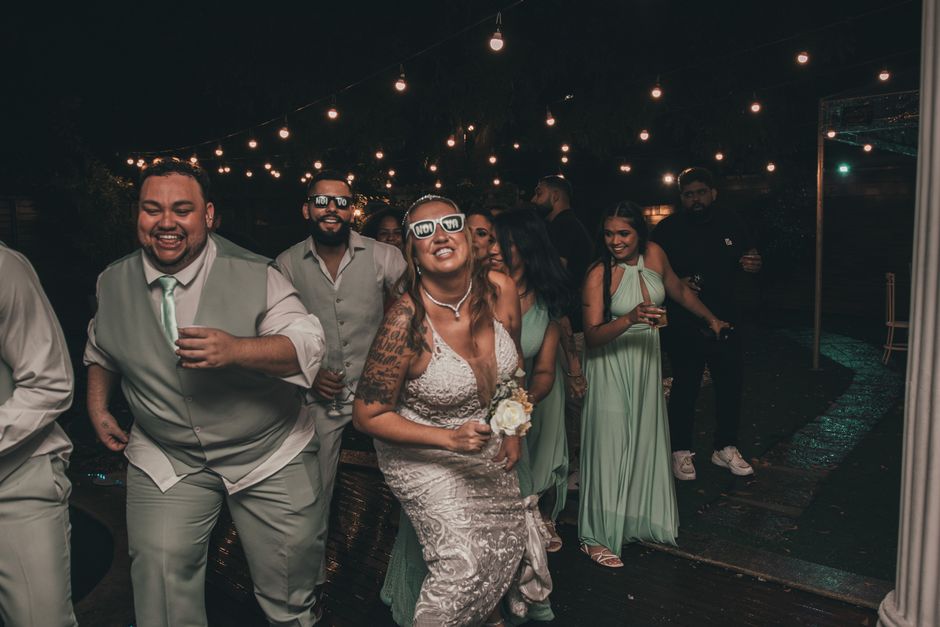 Group of wedding guests dancing joyfully under string lights in an outdoor evening celebration.