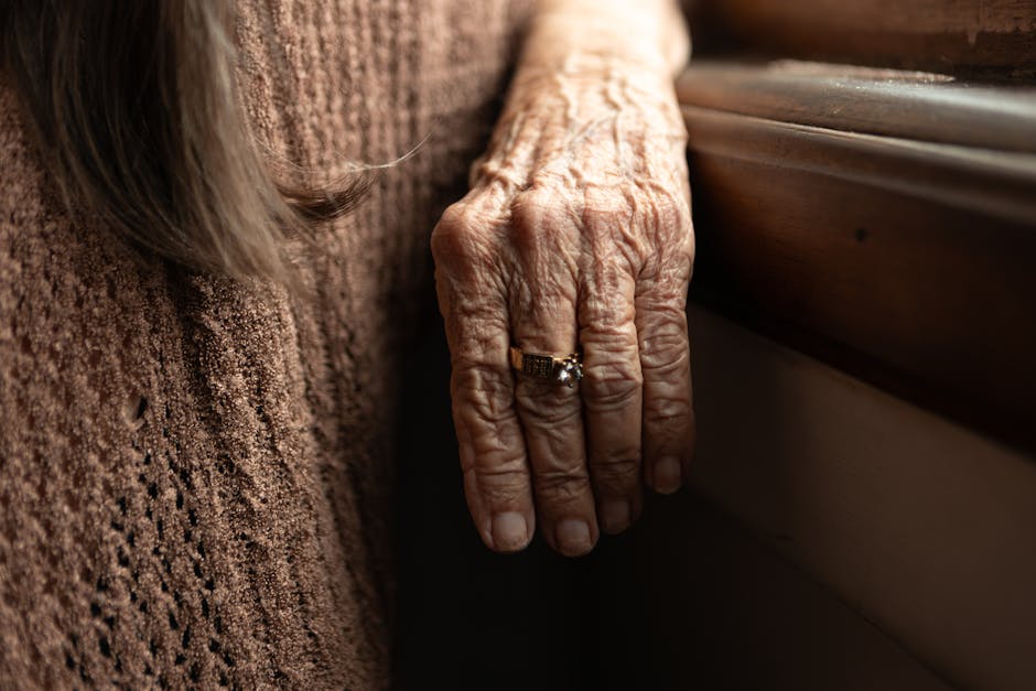 Close-up image of an elderly hand with a ring, showcasing wrinkles and texture against a brown fabric.