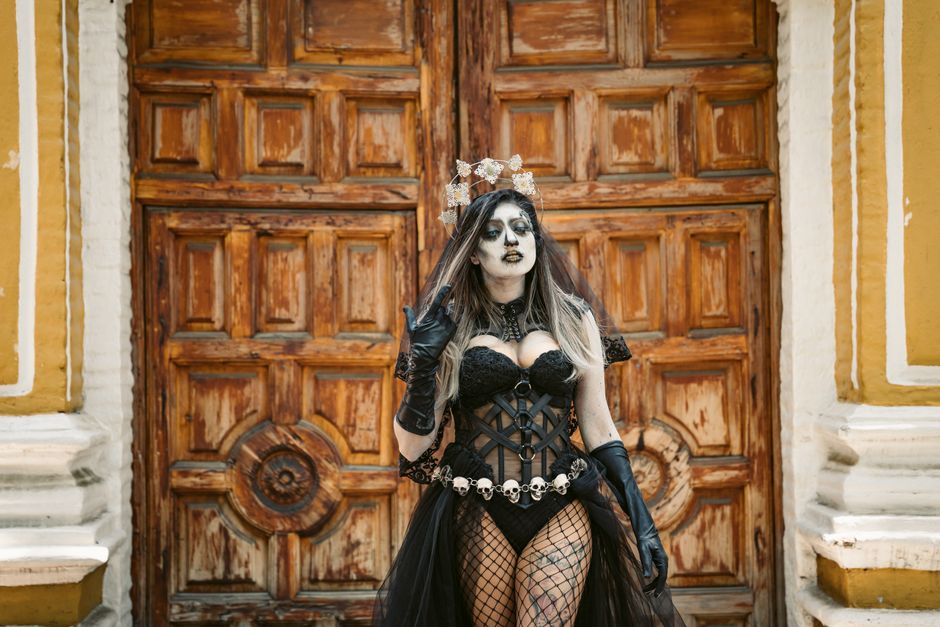 Woman in traditional Day of the Dead costume standing before ornate wooden door in Mexico City.