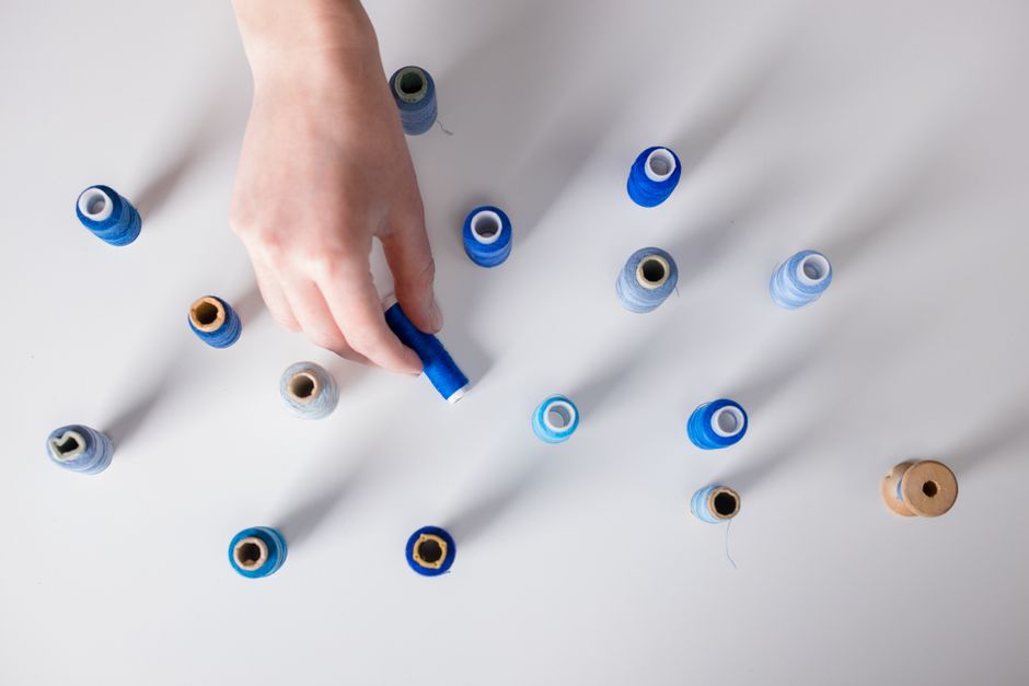 Hand arranging colorful sewing threads on a white surface, capturing creativity and order.