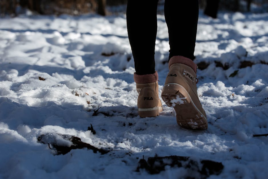 Person walking in brown boots on a snow-covered forest path, captured from behind.