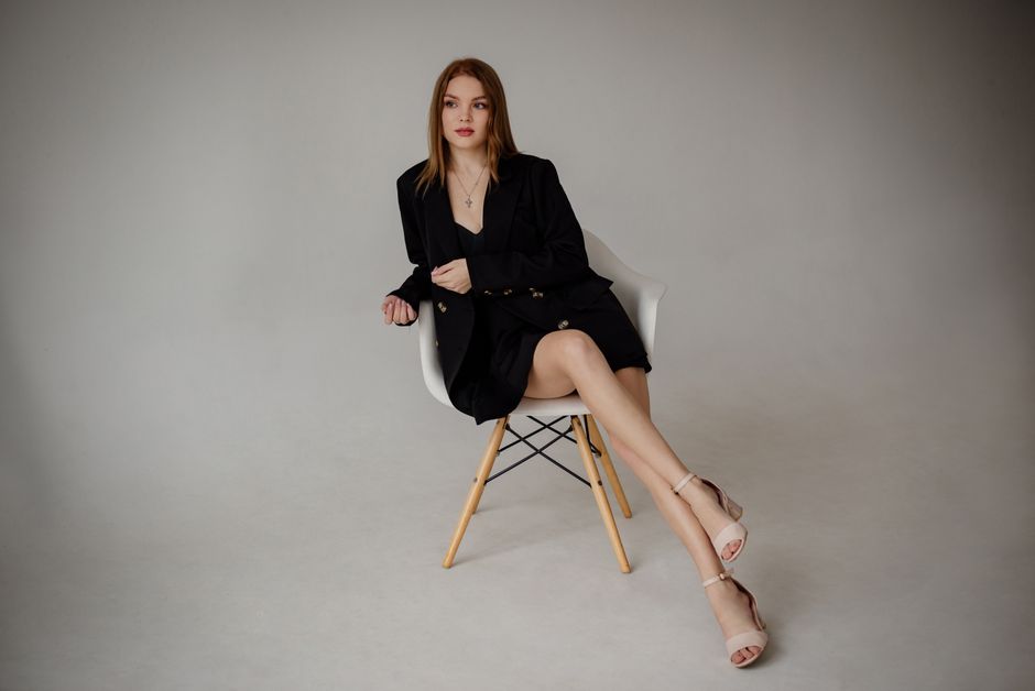 Sophisticated fashion portrait of a woman in a black suit sitting on a modern chair.