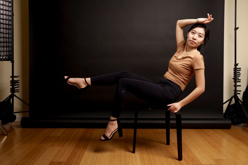 Studio portrait of a woman posing on a stool with a black background.