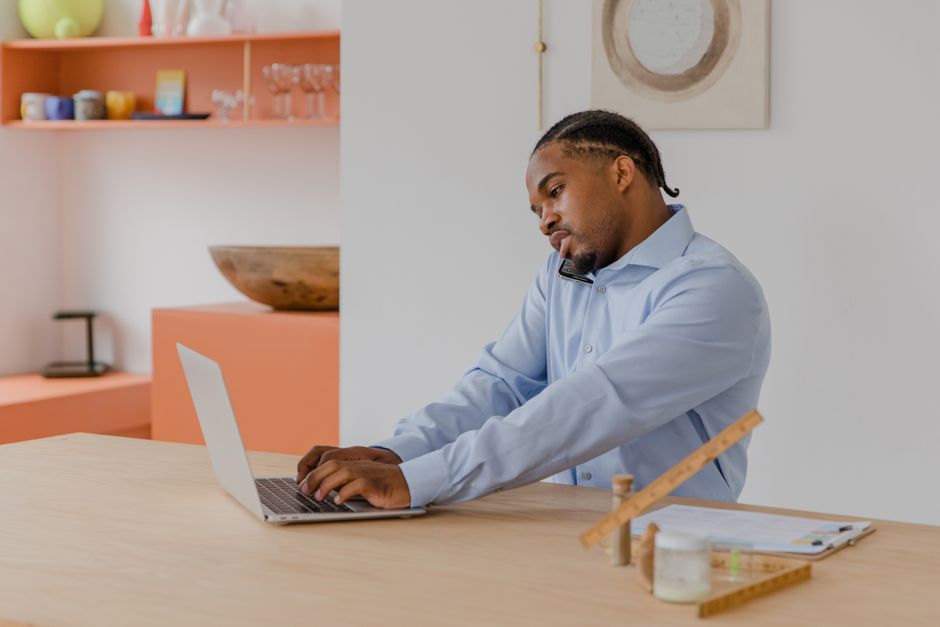 Focused businessman using a laptop and phone simultaneously, working in a modern office space.