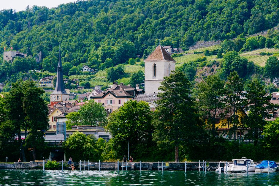 Charming Swiss village nestled by a lake with lush green hills and historic architecture.