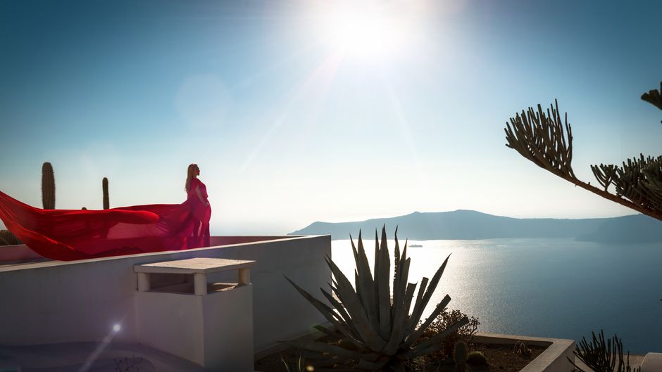 A woman in a red dress poses with a view of Santorini's stunning seascape.