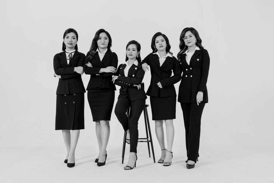 Group of professional women in black suits posing confidently in a studio setting.