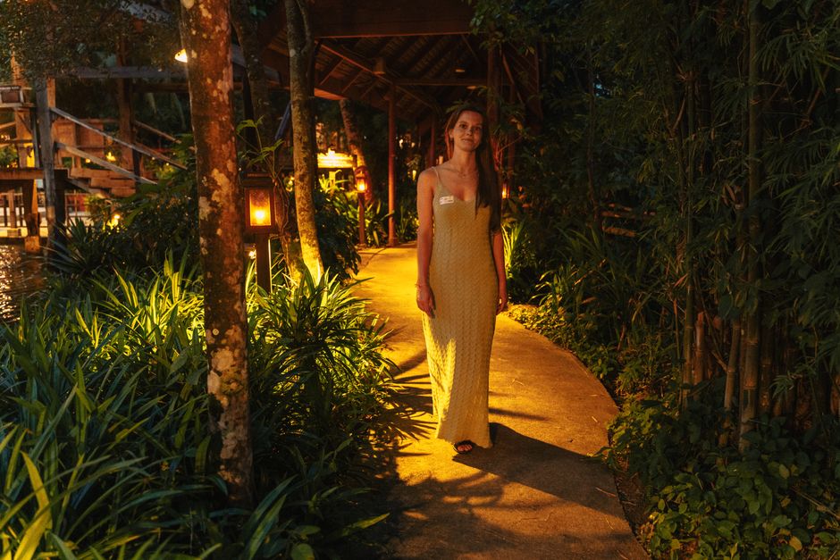 A woman in a yellow dress walks through a tropical garden path, illuminated at night.