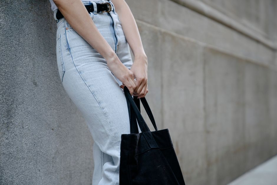 Crop anonymous female in casual jeans and with black eco friendly bag standing near wall in city street