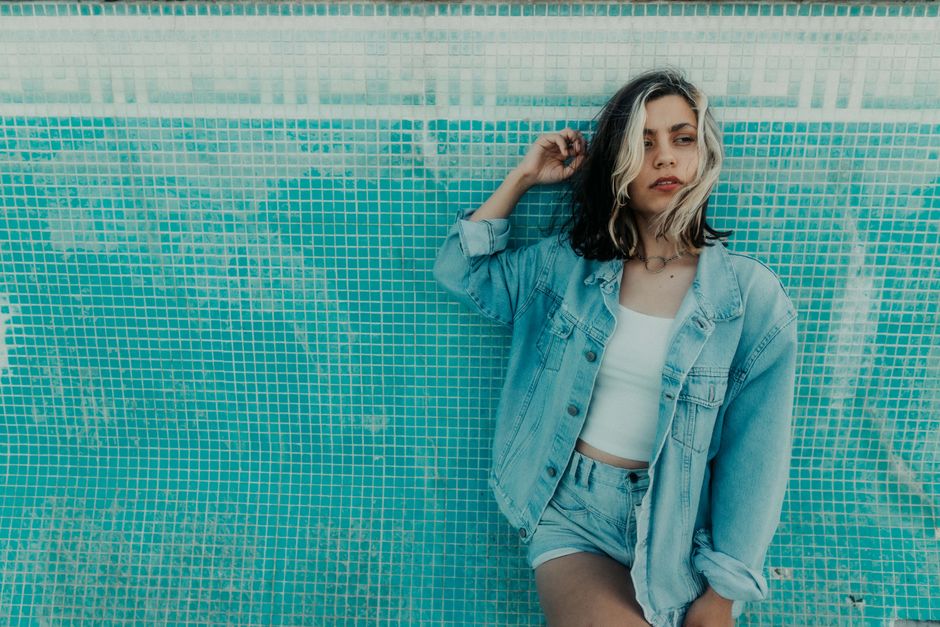 Stylish woman in denim jacket poses confidently against a textured mosaic wall.
