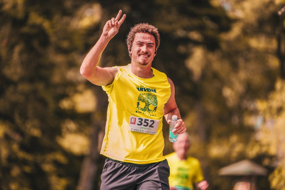 A cheerful man in a yellow shirt runs a marathon, showing a peace sign.