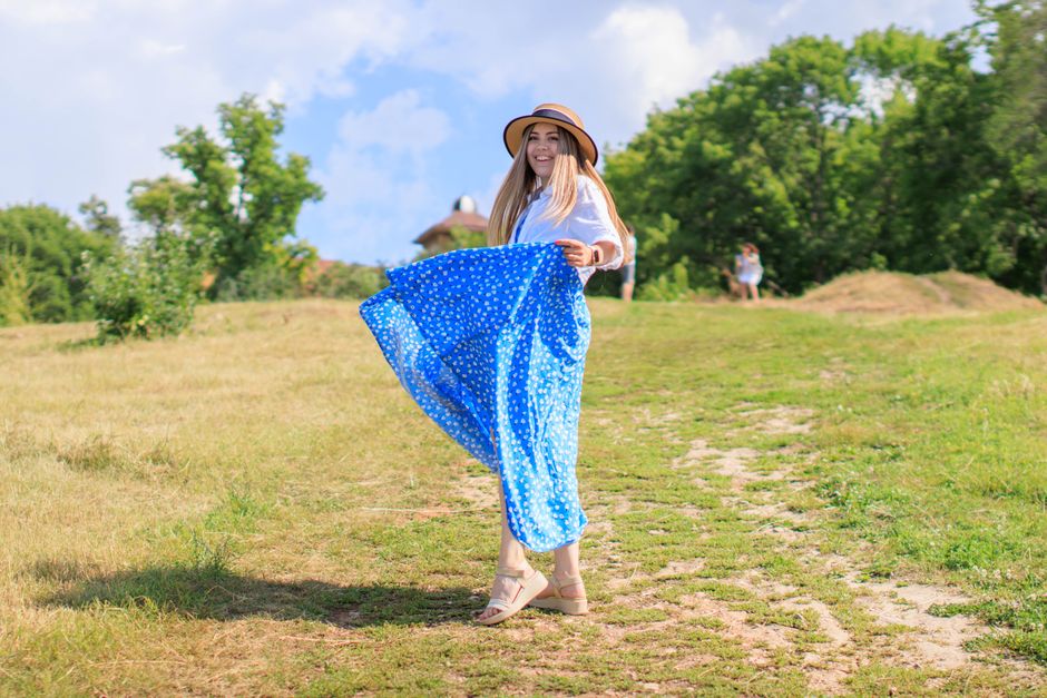 Smiling woman in a blue polka dot dress on a sunny day outdoors.