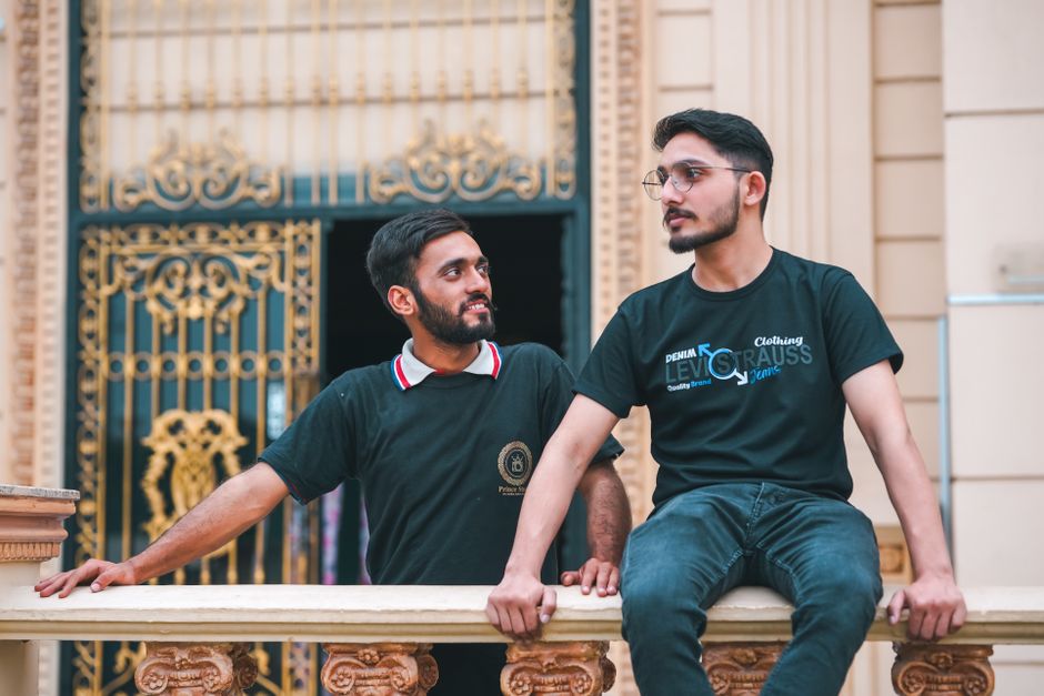 Two young men in casual outfits enjoying a moment on a decorative palace balcony.