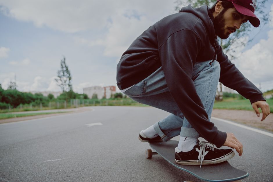 A young man enjoying skateboarding on a smooth road under a bright, clear sky.