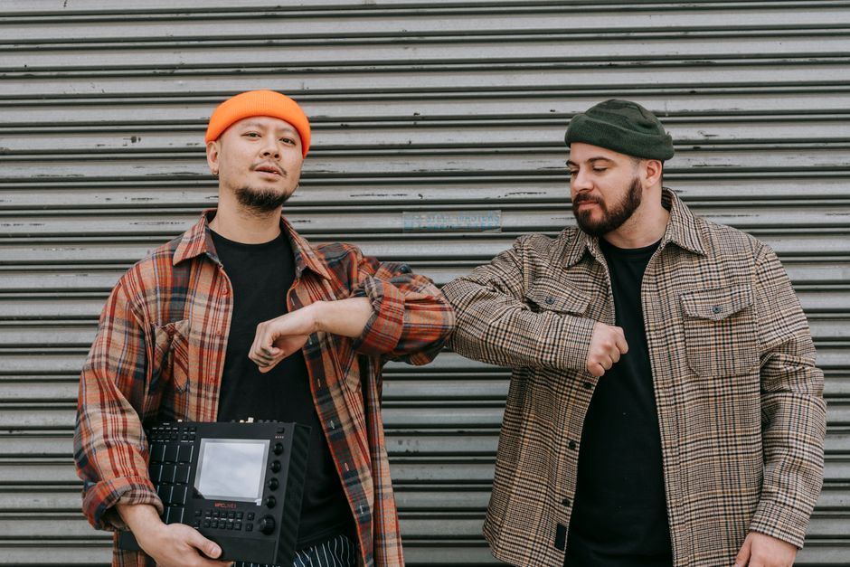 Two men in plaid shirts and beanies greeting with an elbow bump outdoors.