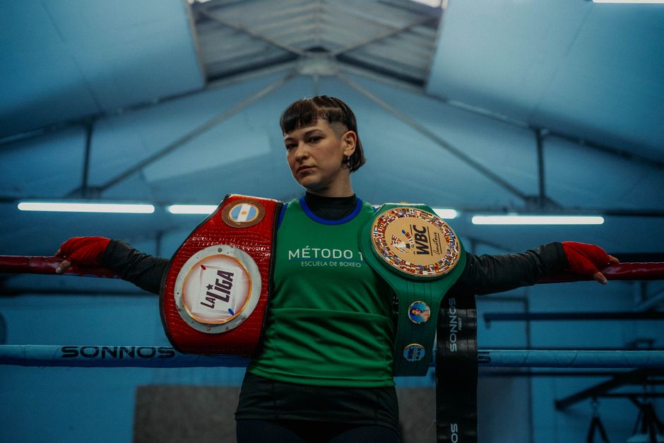 A female boxer standing in a boxing ring with championship belts in Buenos Aires gym.