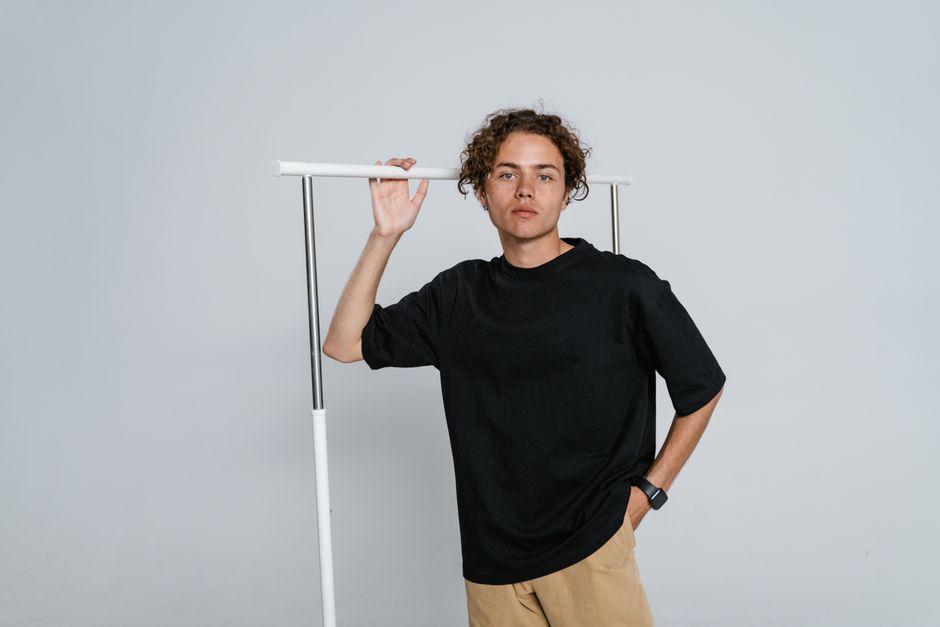 Young male model in casual attire posing in a minimalist studio setting with a white background.