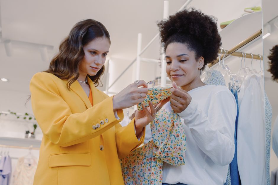Two women shopping fashionably at a boutique, choosing colorful dresses indoors.