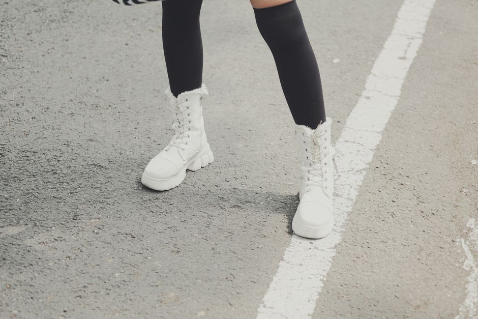 Close-up of stylish white boots on a city road, featuring black knee-high socks.