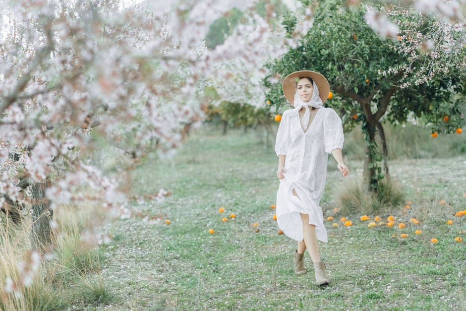 A woman in a white dress and hat walks through a cherry blossom orchard, creating a serene springtime scene.